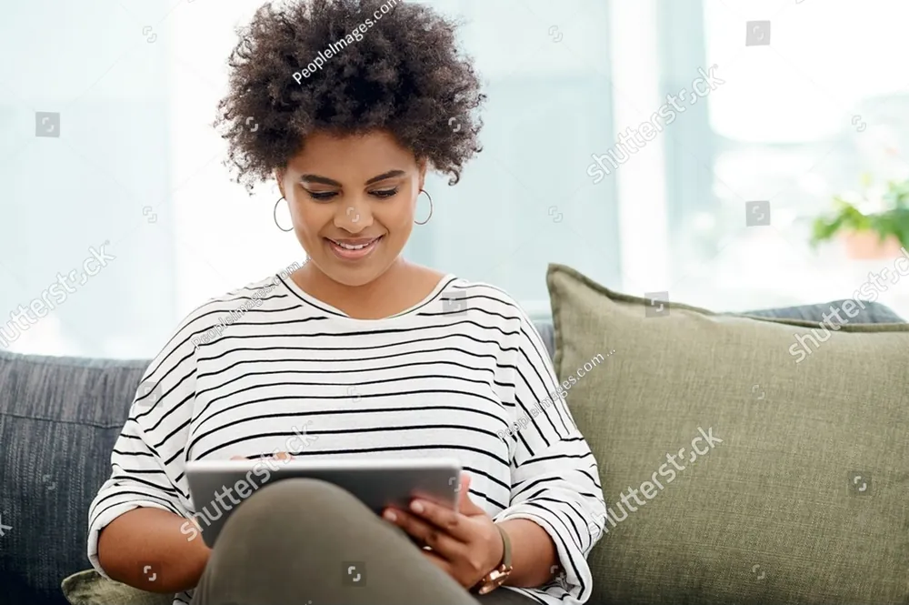 A smiling woman with curly hair reading a tablet on a sofa