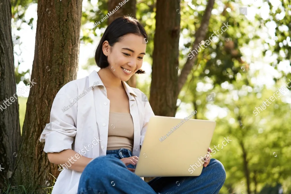 A smiling woman working on a laptop under the trees