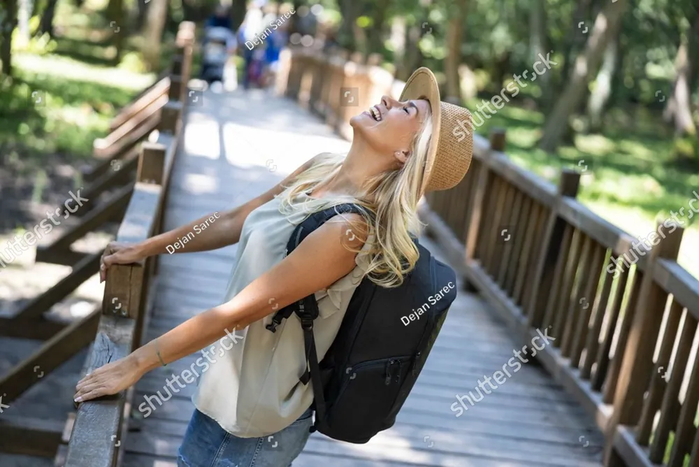 A woman with a backpack leaning back and laughing on a forest boardwalk
