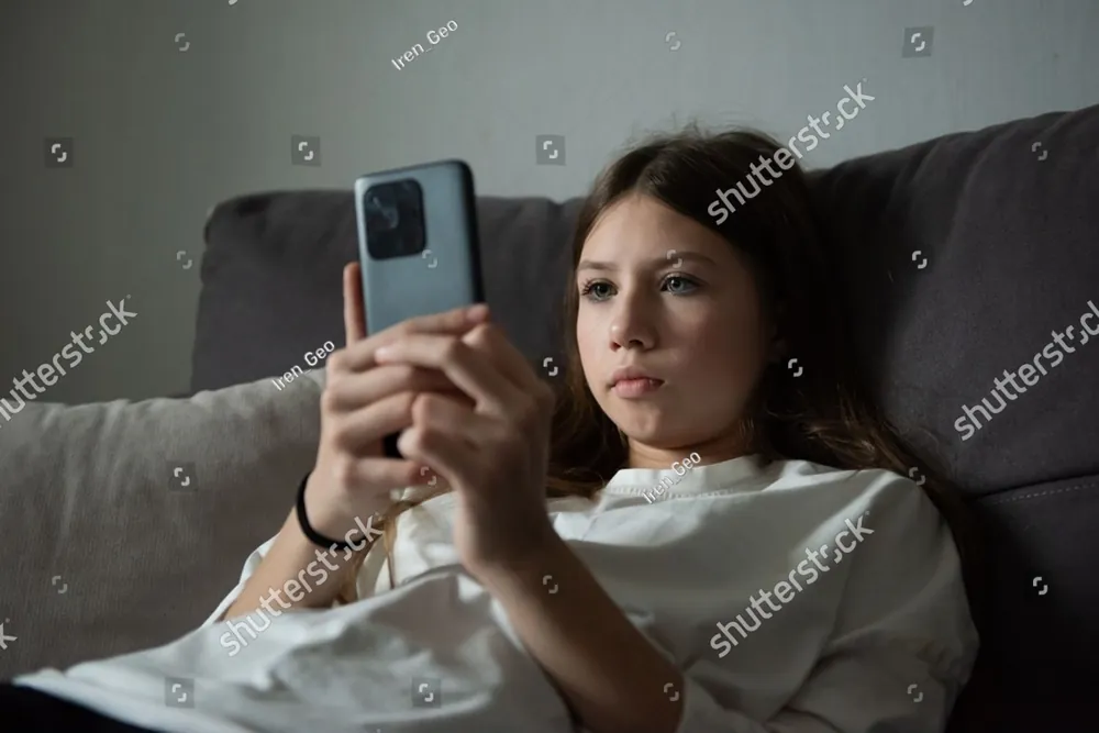 A teenage girl lying on a sofa, looking at her phone