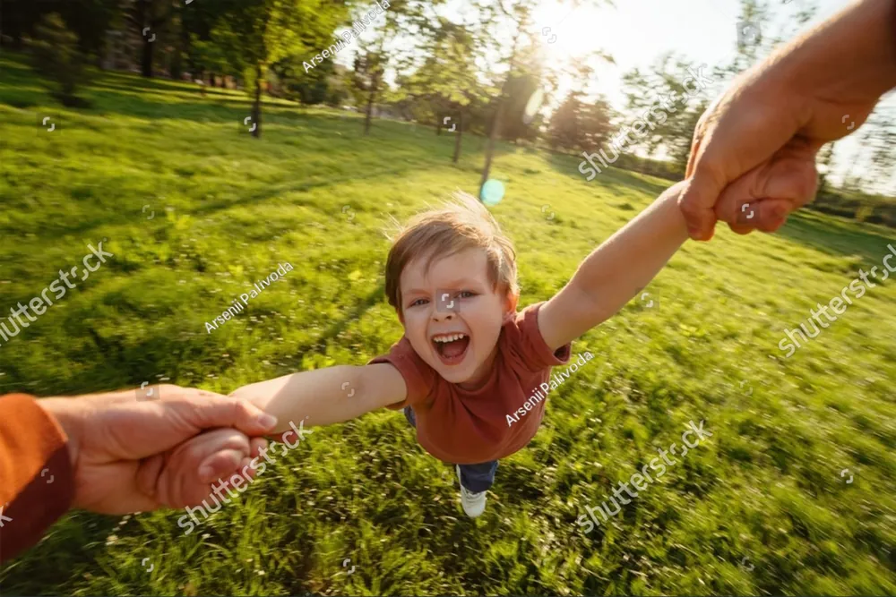 A laughing child swung by the hands over the grass