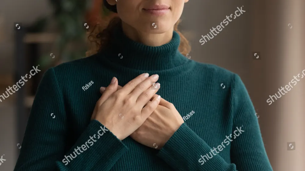 A woman in a green sweater with her hands on her chest